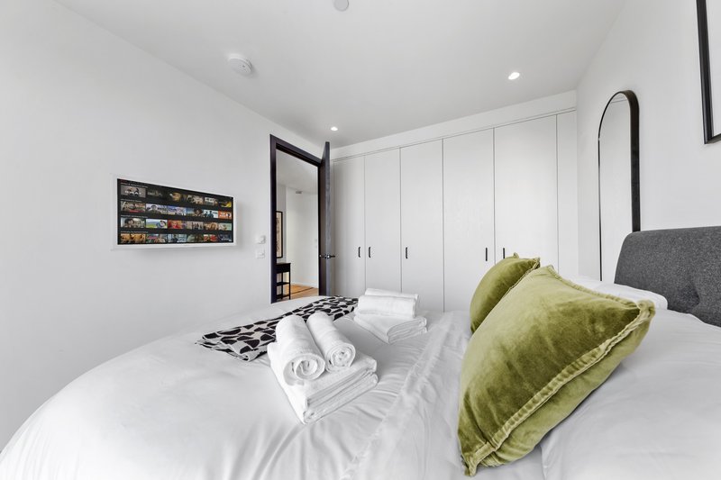 Modern bedroom with double bed, white bedding, green cushions and built-in wardrobes