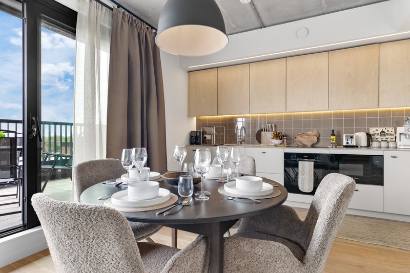 Modern open-plan kitchen and dining area with round table, grey chairs, and balcony access