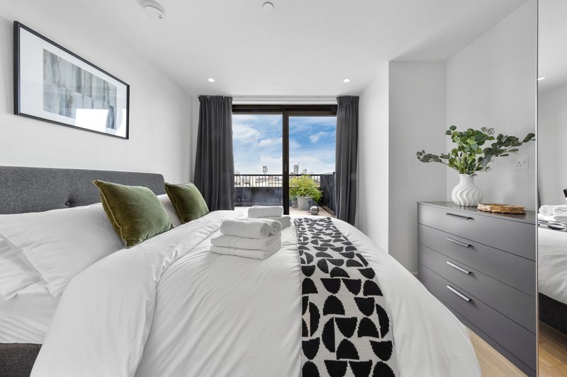 Modern bedroom with double bed, green pillows, grey headboard and city view from balcony