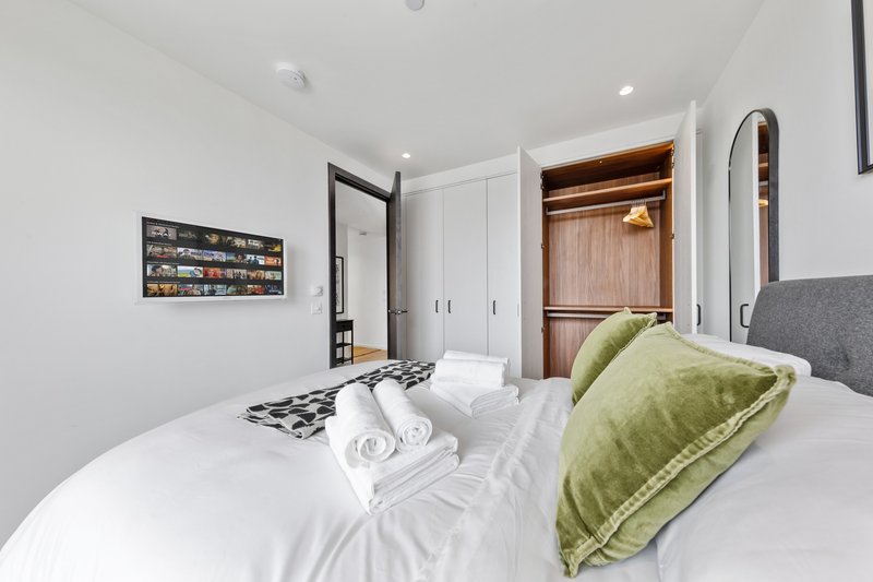 Modern bedroom with white bedding, green pillow, gray headboard and wooden wardrobe