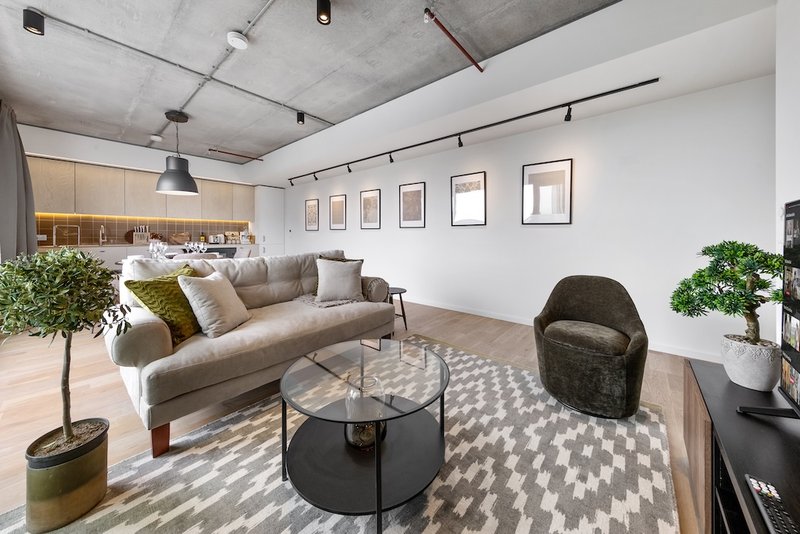 Modern open-plan living area with beige sofa, black armchair, glass coffee table and potted plants