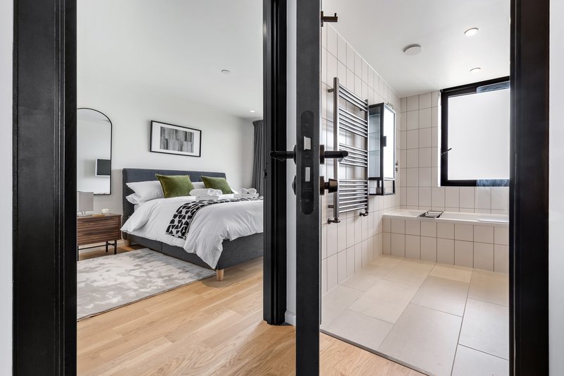 Modern bedroom and ensuite bathroom separated by black framed glass doors