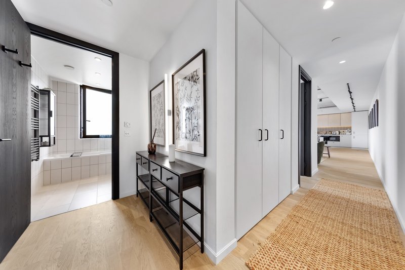 Modern hallway with wooden flooring, white walls, console table, and open bathroom view
