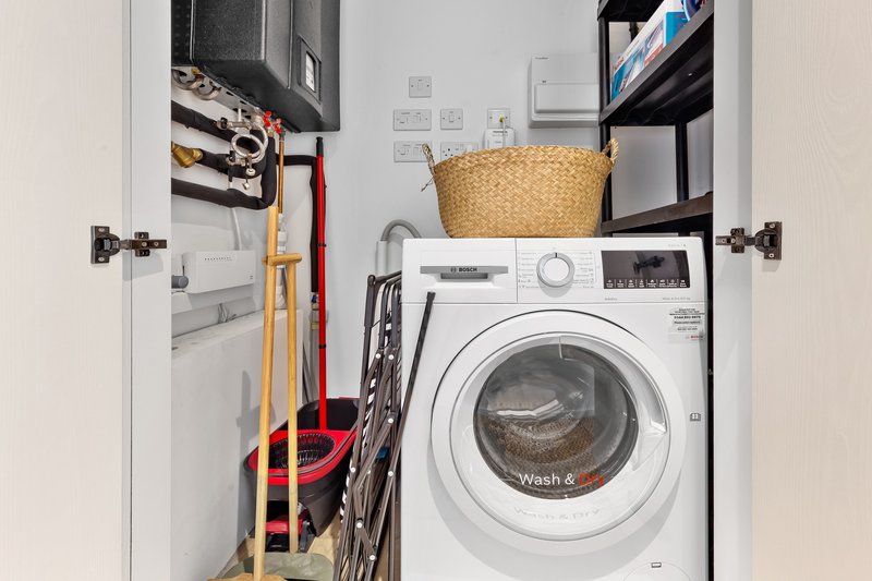 Utility closet with white washing machine, wicker basket, cleaning supplies and tools