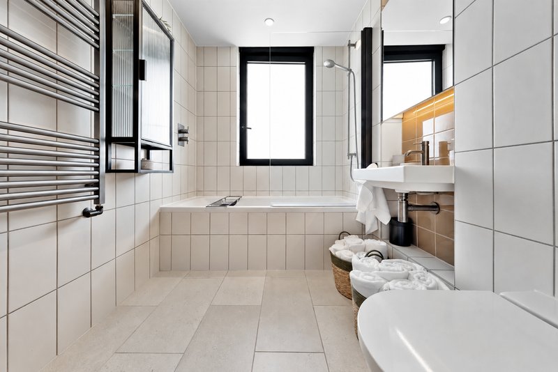 Modern bathroom with white tile, double sink vanity, towel rail and window