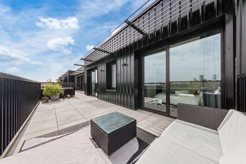 Modern rooftop terrace with seating, glass table, black railings and city views