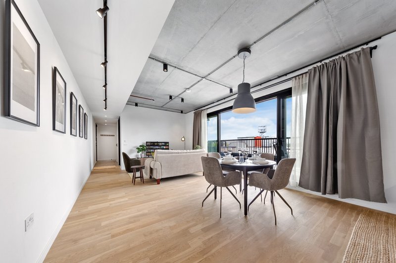 Modern open-plan apartment with dining table, sofa, and floor-to-ceiling windows overlooking city