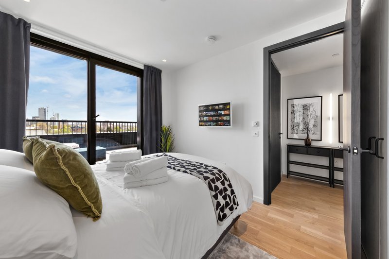 Modern bedroom with double bed, white bedding, gold cushion, wood flooring and city view.