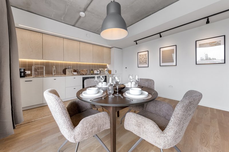 Modern dining area with round table, upholstered chairs, and open-plan kitchen with pendant lighting.