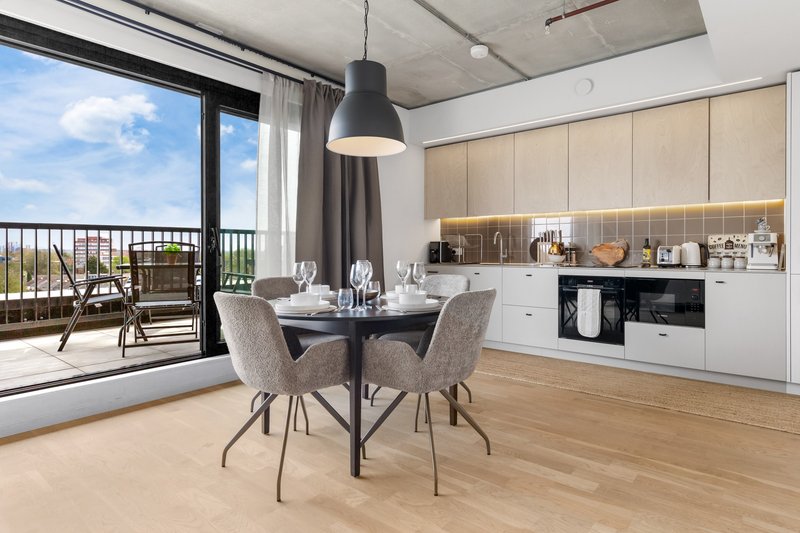 Modern open-plan kitchen and dining area with round table, chairs, pendant light and balcony view