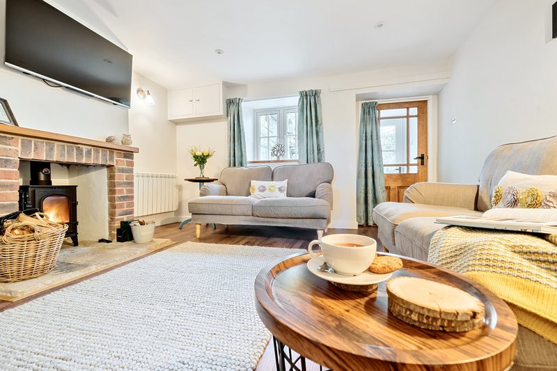 Bright open-plan living area with fireplace, sofa, bed, and wooden dining table with cup