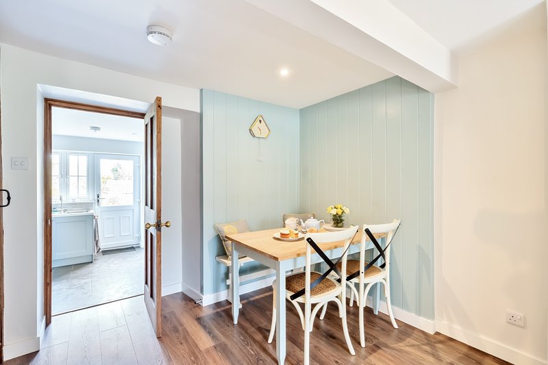 Bright dining nook with wooden table, white chairs, light blue wall panelling and open doorway