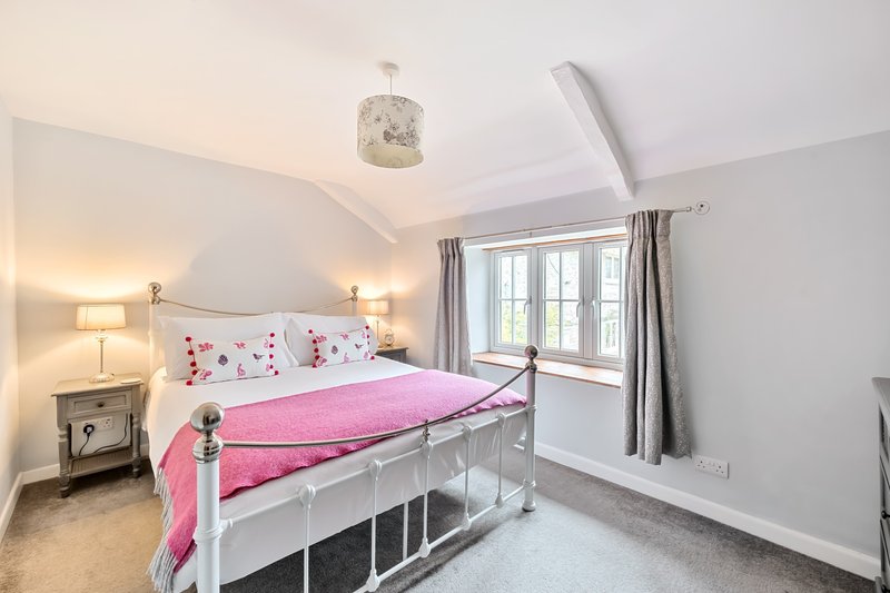 Bright bedroom with white metal bed frame, pink bedding, twin lamps, and large window with grey curtains
