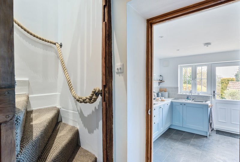 Hallway with rope detail, wooden beams, and view into bright kitchen with blue cabinetry