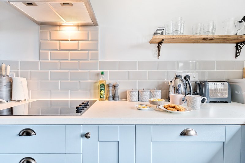 Modern kitchen with light blue cabinetry, white countertop, subway tile backsplash and wooden shelf