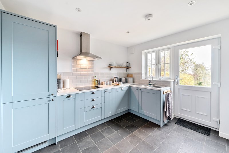 Modern kitchen with light blue cabinetry, subway tile backsplash, and garden view through patio doors
