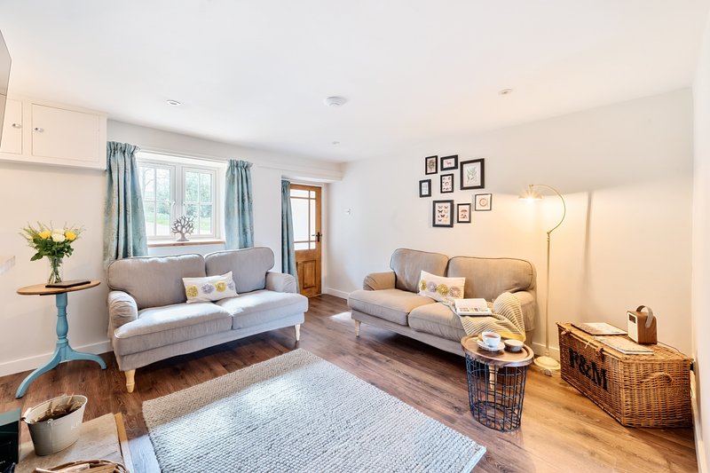 Bright living room with two grey sofas, framed wall art, window with blue curtains, and wooden flooring