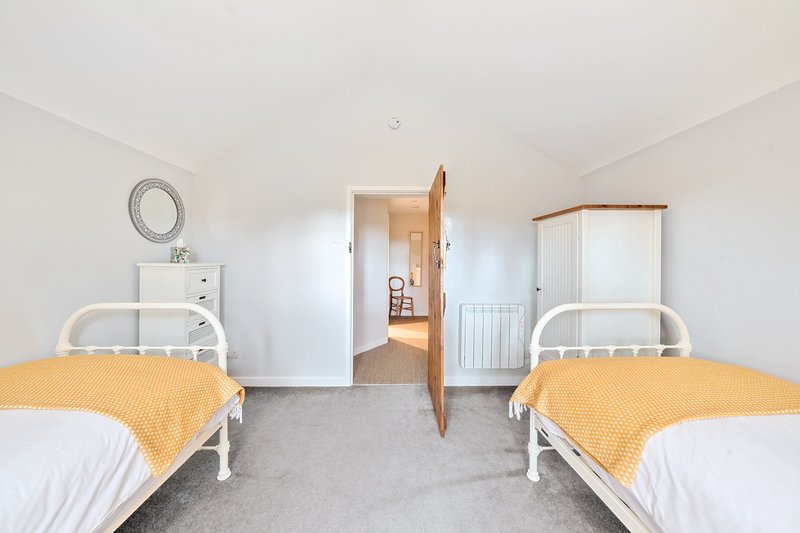 Bright twin bedroom with two single beds, white metal frames, yellow throws, and connecting door to hallway