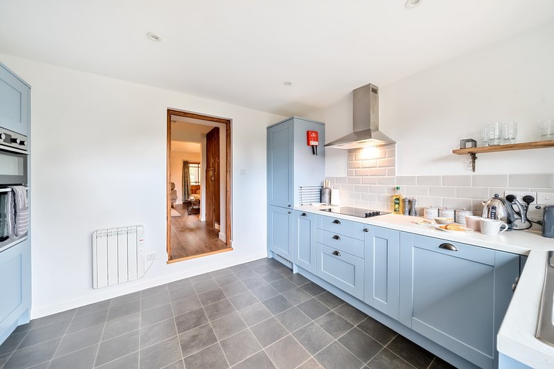 Modern kitchen with blue cabinetry, white subway tiles, stainless steel hood, and gray tile flooring
