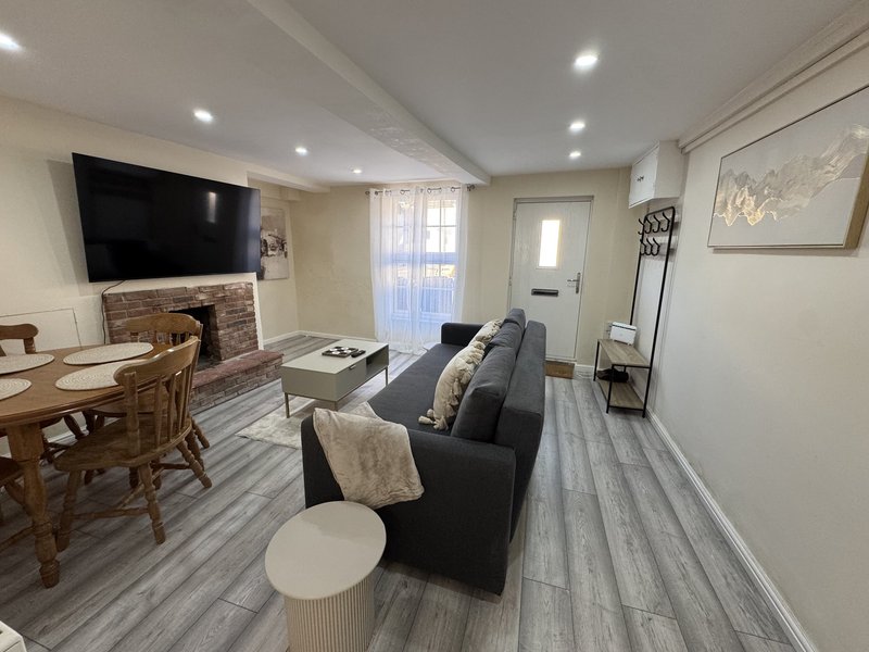Open-plan living room with dark sofa, dining table, mounted TV, and fireplace
