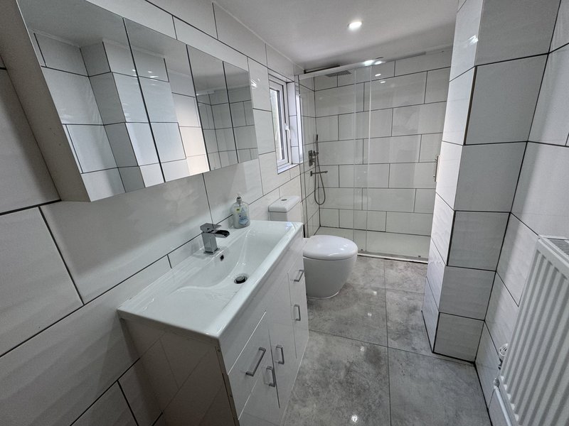 Modern bathroom with white tile walls, vanity sink, toilet, and walk-in shower enclosure