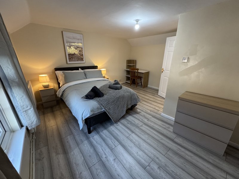 Spacious bedroom with double bed, wooden flooring, bedside lamps, and grey dresser