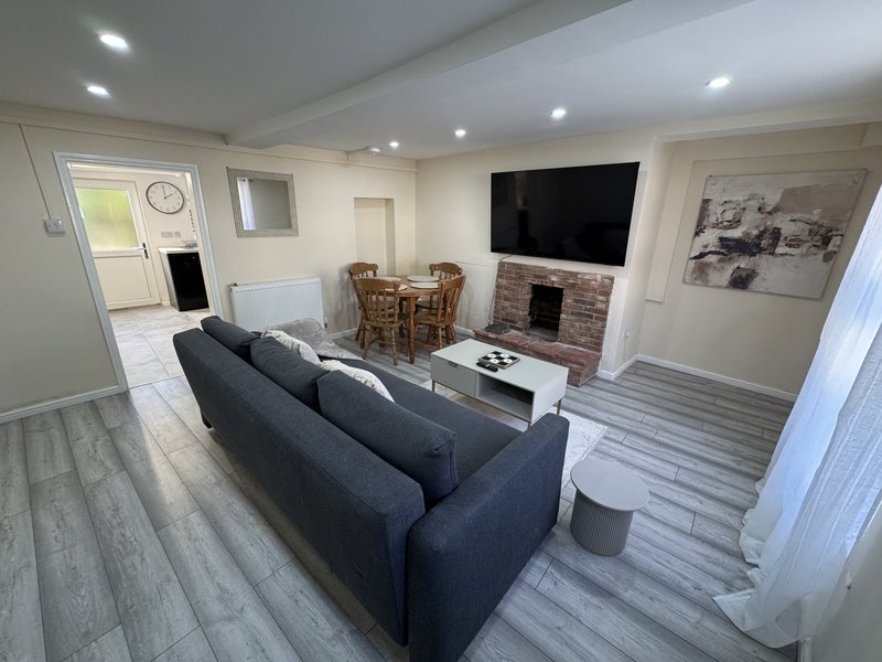 Open-plan living room with dark sofa, wall-mounted TV, fireplace and wooden dining table