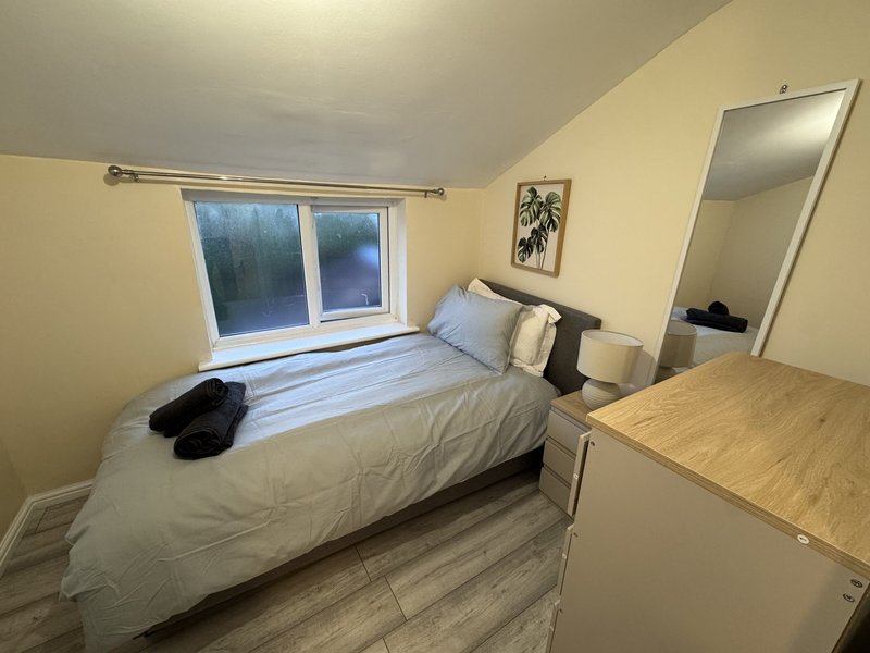 Bedroom with single bed, wooden desk, large window and mirror on wall