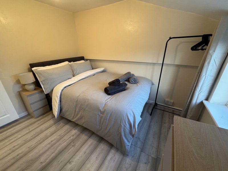 Bedroom with double bed, pillows, folded clothes, wooden flooring and clothing rack