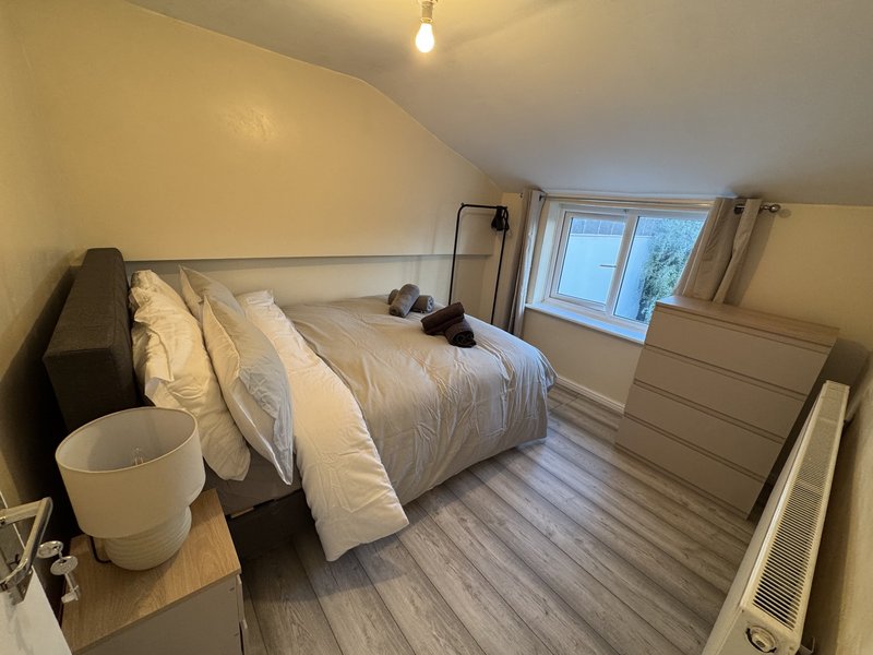 Bright attic bedroom with double bed, wooden flooring, dresser and window
