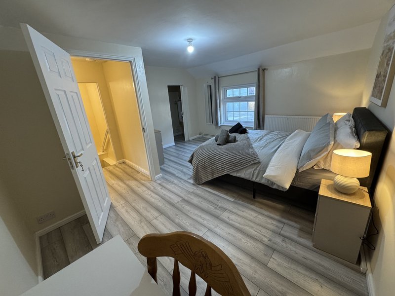 Spacious bedroom with double bed, wooden flooring, bedside lamps, and open doorway to ensuite