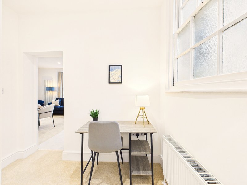 Bright modern hallway with small desk, chair, potted plant and framed artwork on wall