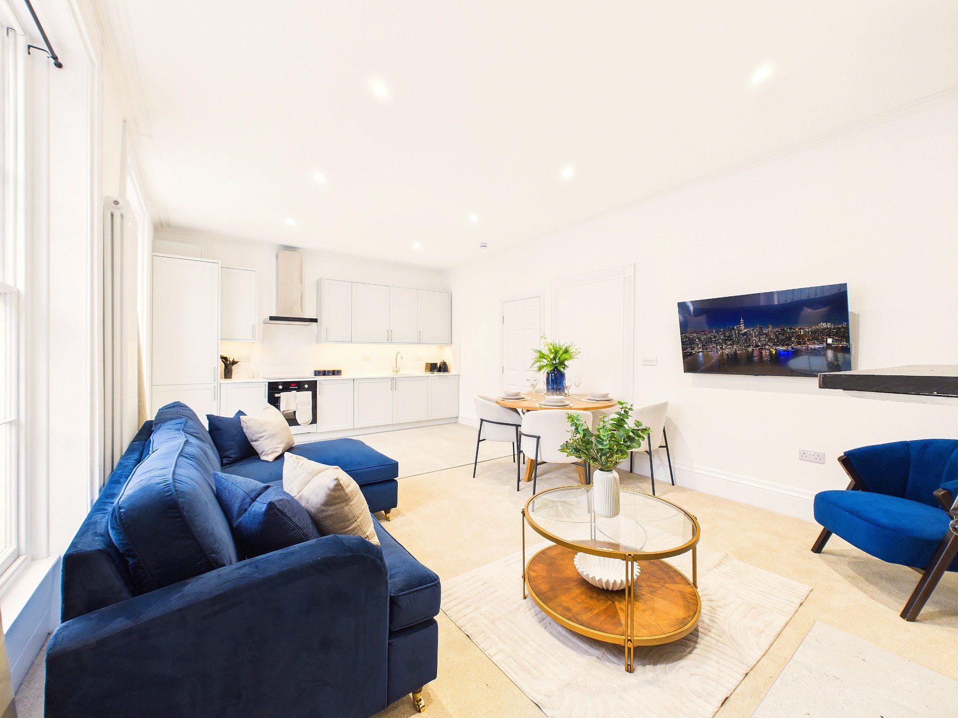 Modern open-plan living room with blue sofa, dining area, kitchen, and city skyline artwork on wall