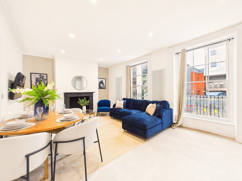 Bright open-plan living room with blue sofa, wooden dining table, fireplace and large windows