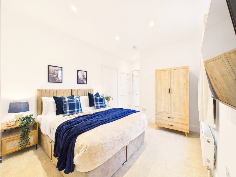 Bright modern bedroom with double bed, blue bedding, wooden wardrobe and framed wall art