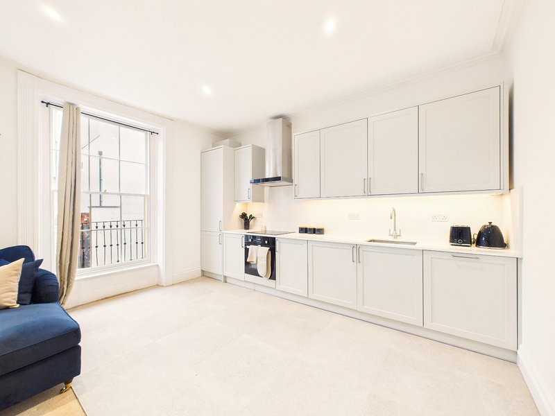 Modern open-plan kitchen and living area with white cabinetry, stainless steel appliances, and blue sofa