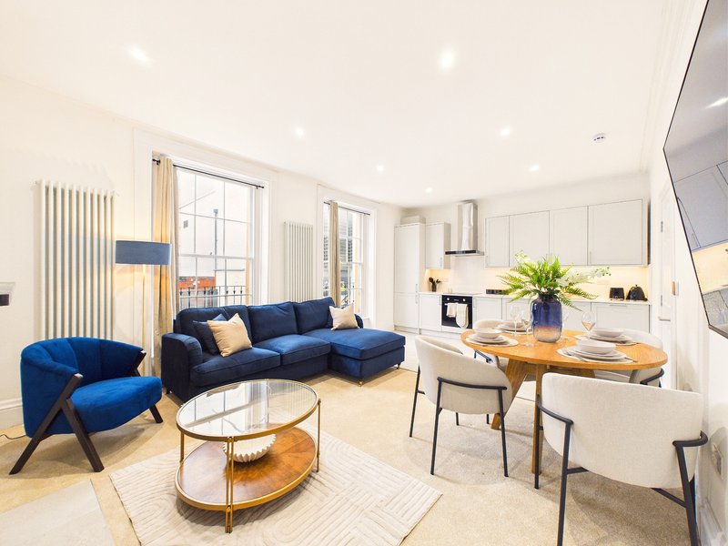 Modern open-plan living room with blue sofa, armchair, wooden dining table and kitchen area