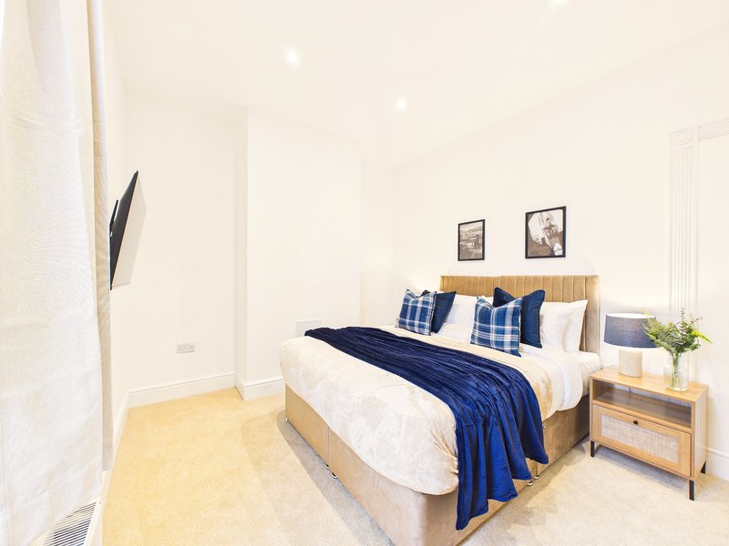Modern bedroom with double bed, blue throw, wooden headboard and nightstand