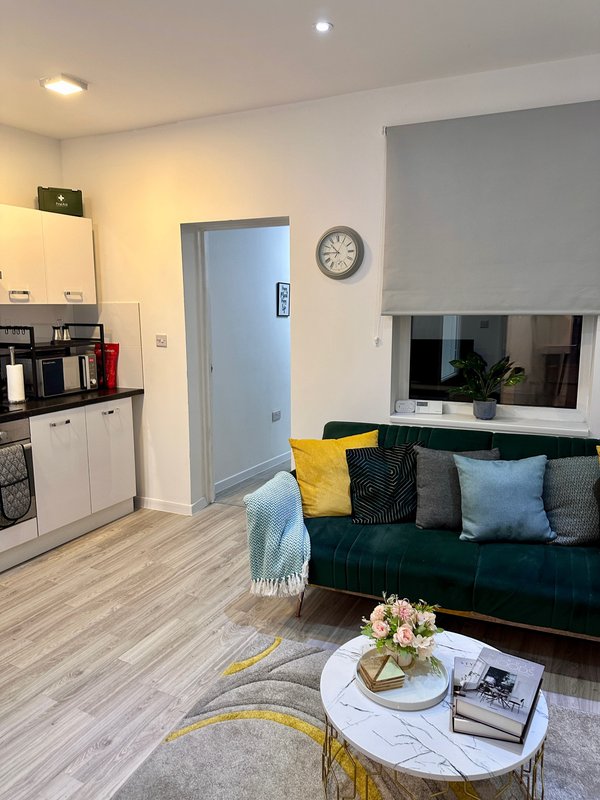 Open-plan living area with kitchen, dark sofa, decorative cushions, and round coffee table