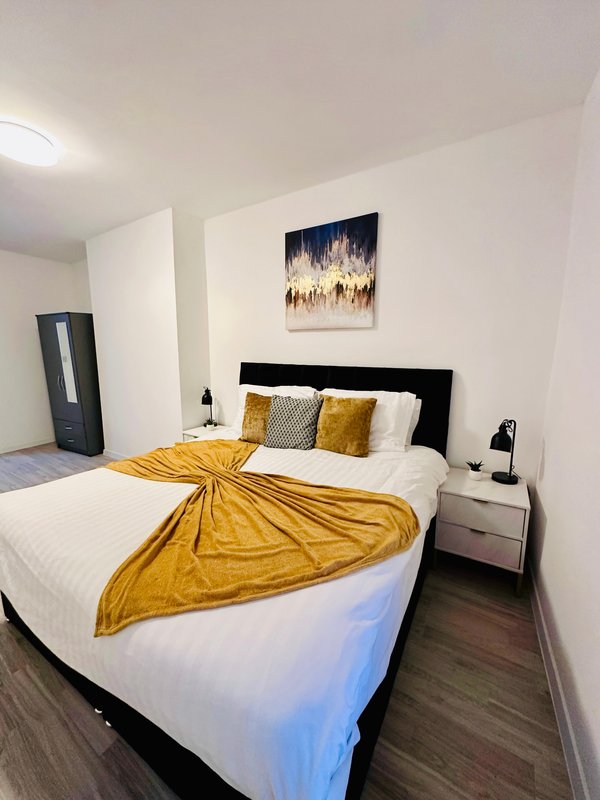 Modern bedroom with double bed, yellow throw, cushions, black headboard and wall art