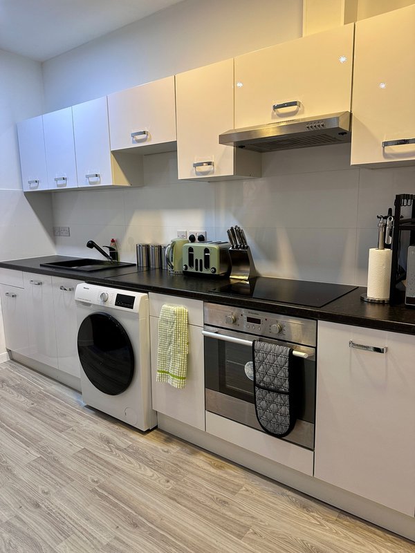 Modern white kitchen with black countertop, integrated appliances, and stainless steel hood