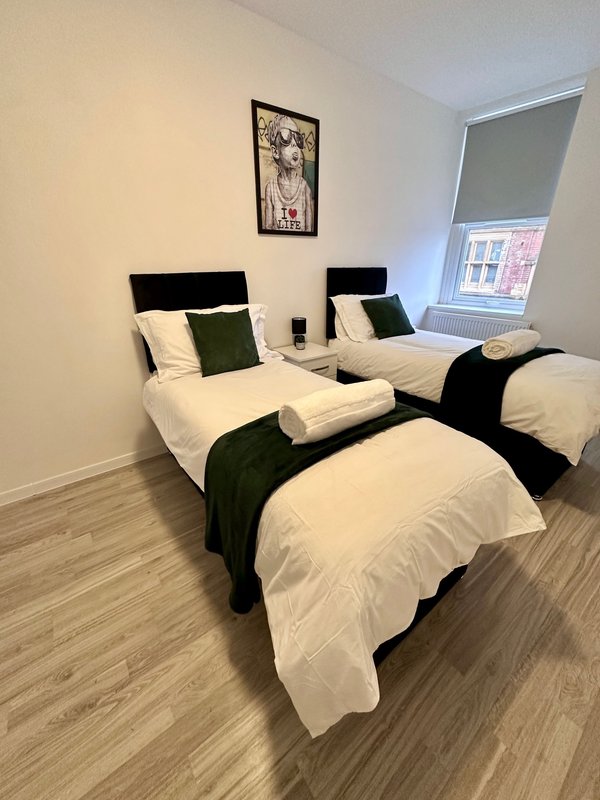 Twin bedroom with white and green bedding, wooden flooring, and wall-mounted artwork
