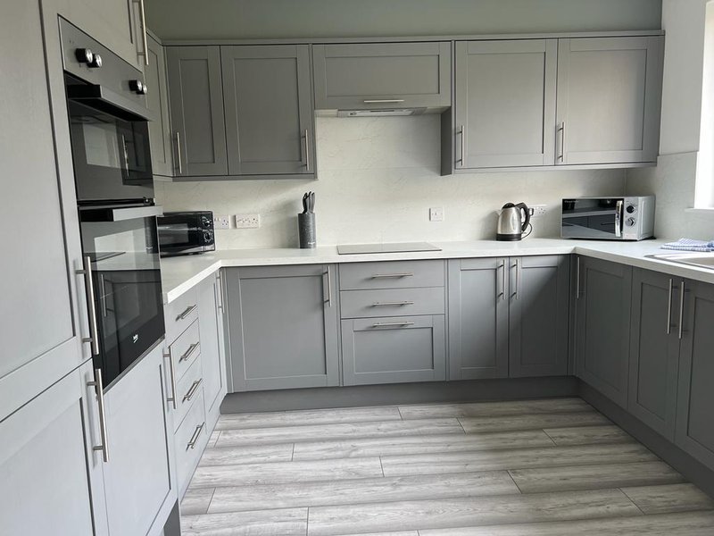 Modern gray kitchen with built-in appliances, white countertops and wood-effect flooring
