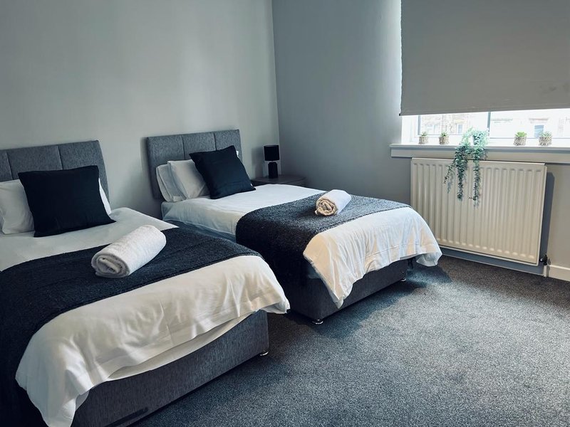 Twin bedroom with two beds, dark headboards, white bedding, radiator and window