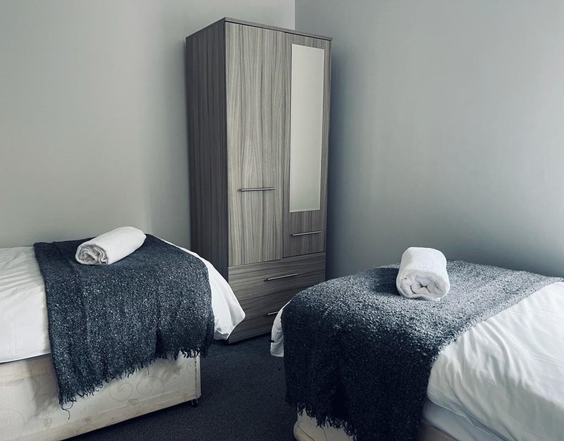 Twin bedroom with two single beds, dark throws, rolled towels, and wooden wardrobe