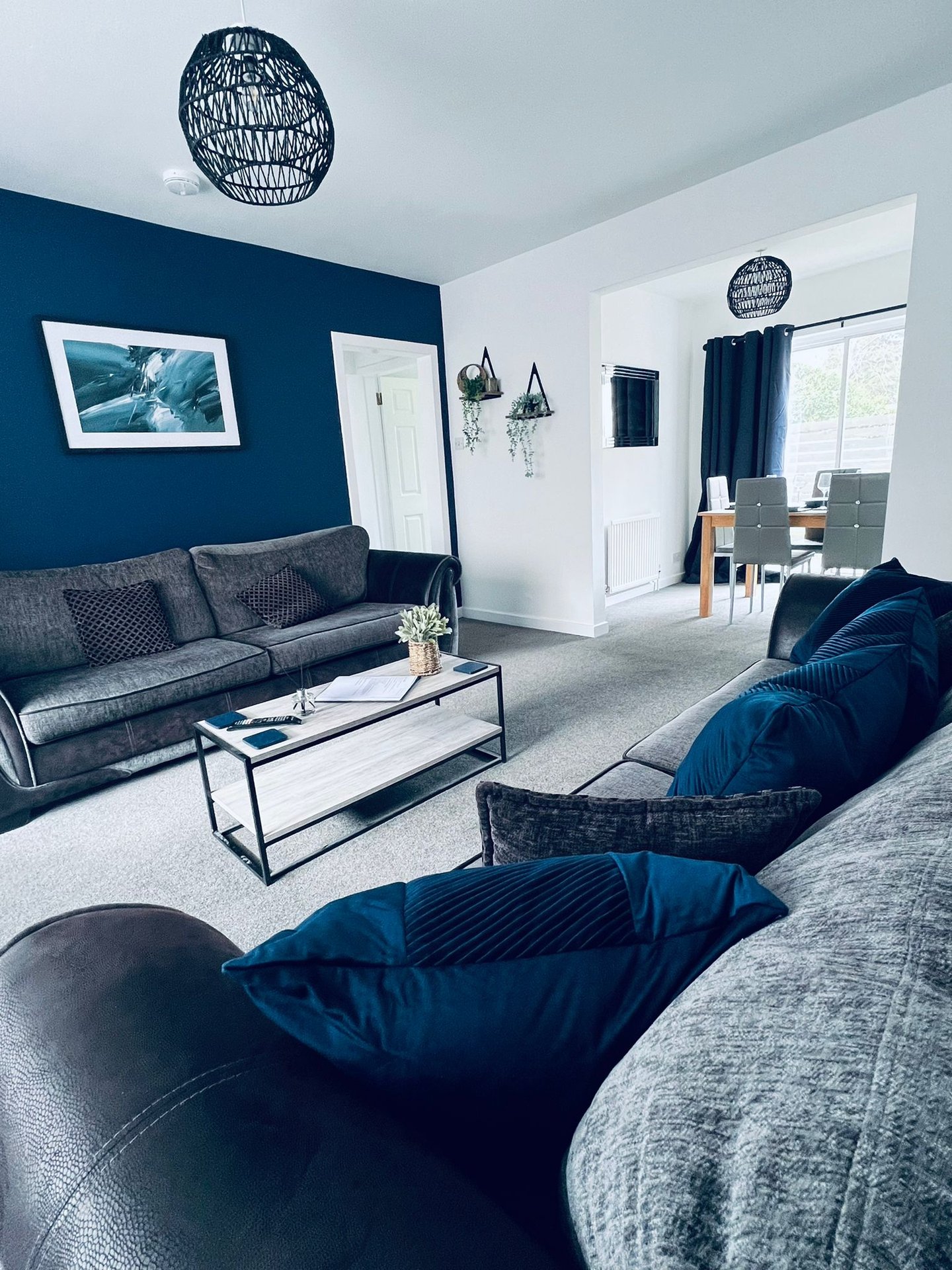 Modern living room with navy accent wall, gray sofa, blue armchair and geometric pendant lights