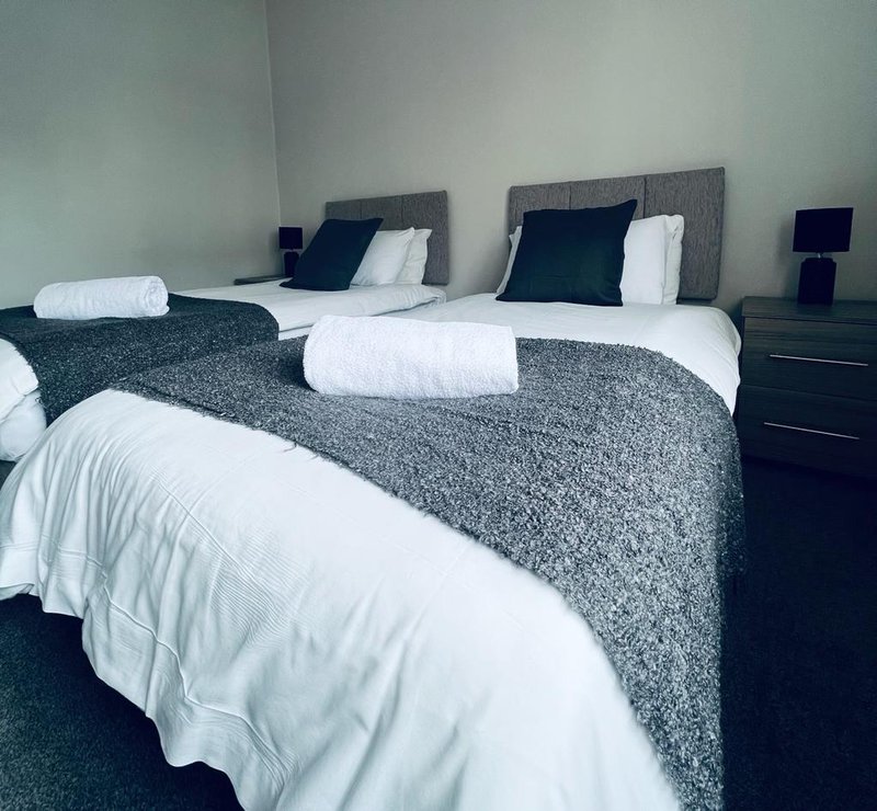 Modern bedroom with three single beds, grey headboards, white pillows and grey throws