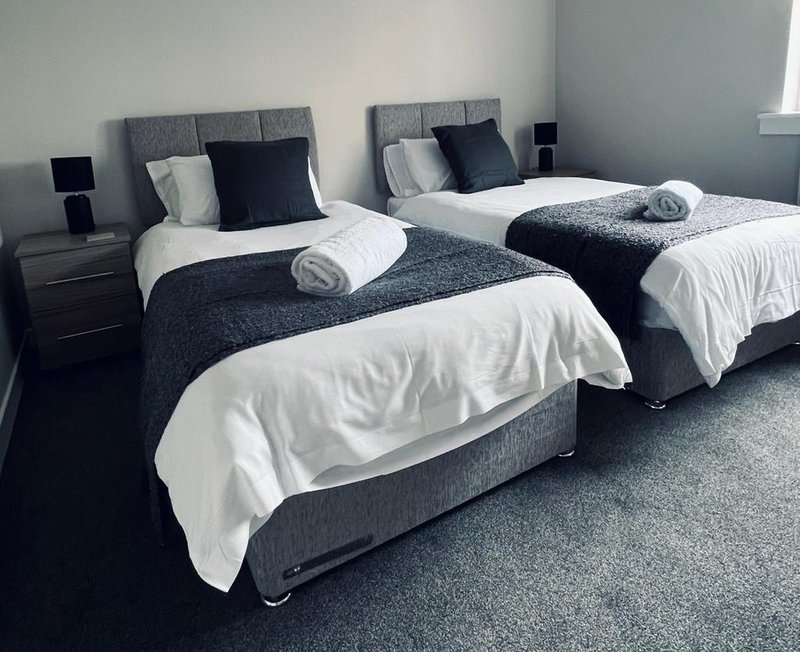 Modern twin bedroom with two single beds, gray headboards, white bedding and rolled towels