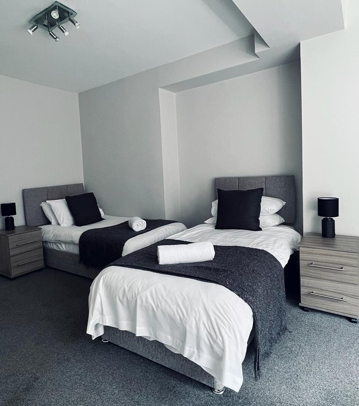 Modern bedroom with three single beds, black and white bedding, grey carpet and minimalist decor