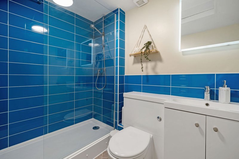 Modern bathroom with blue tile walls, white vanity, toilet, and glass shower enclosure